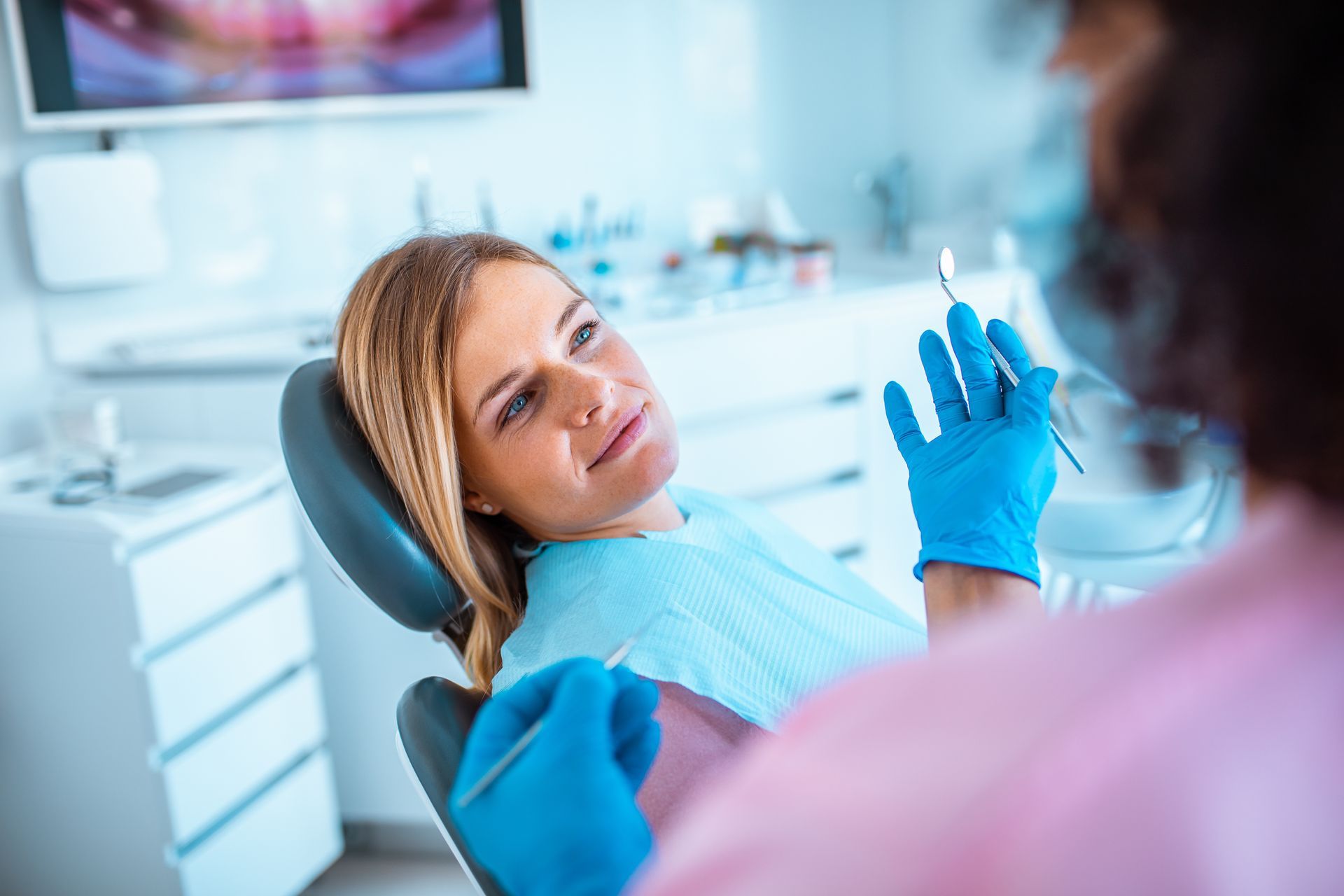 Dentist examining a smiling patient in a dental chair, with blue gloves in a bright clinic