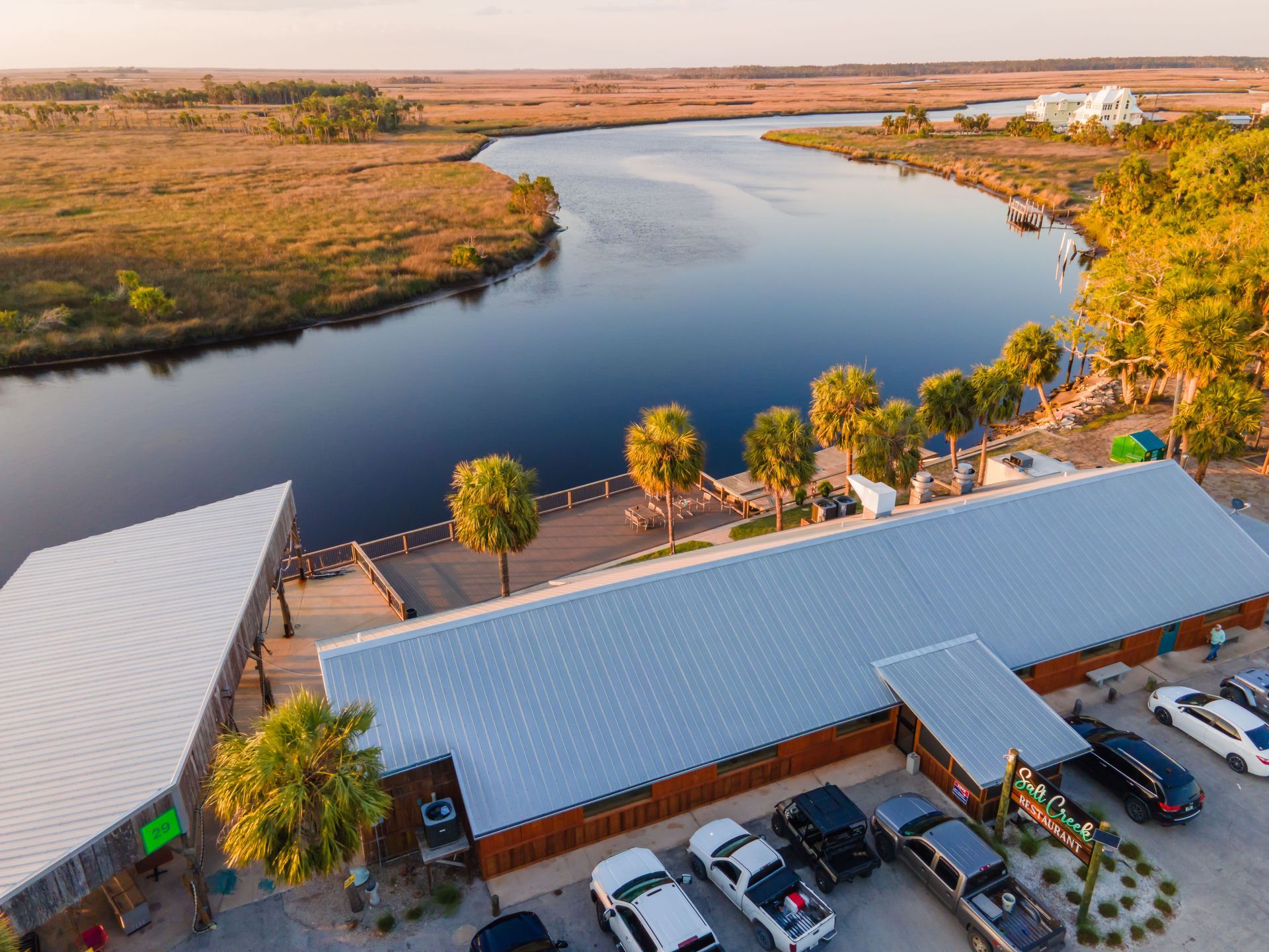An aerial view of a building next to a river with cars parked in front of it.