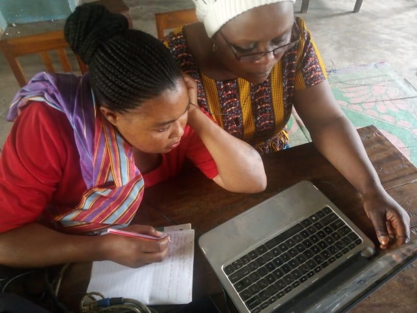 Two people leaning over a laptop and notebook, studying together at a wooden table.