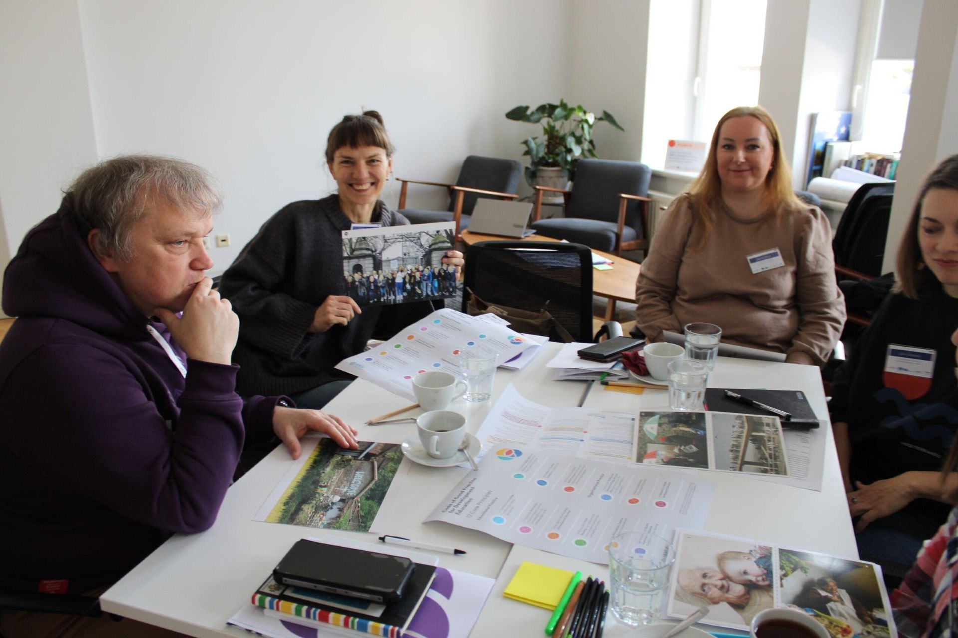 People gathered around a table covered with papers and materials in a bright room
