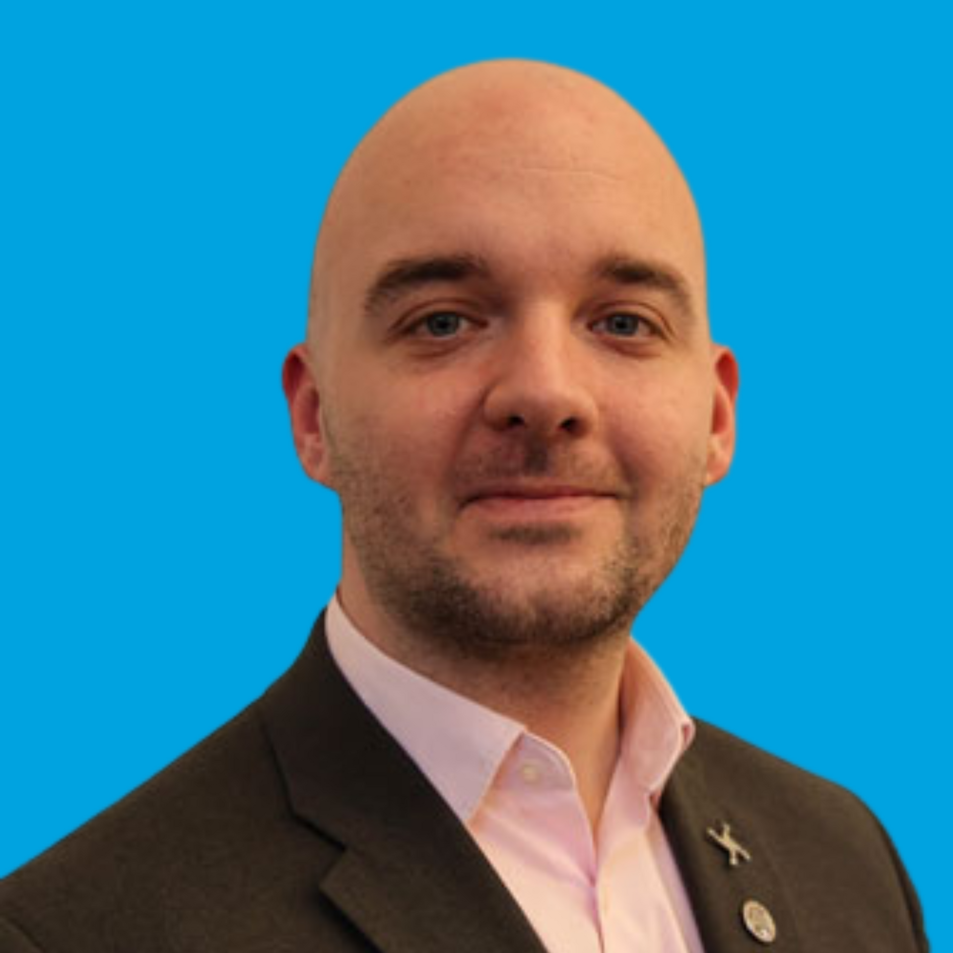 Portrait of a bald man in a dark suit and light pink shirt against a bright blue background