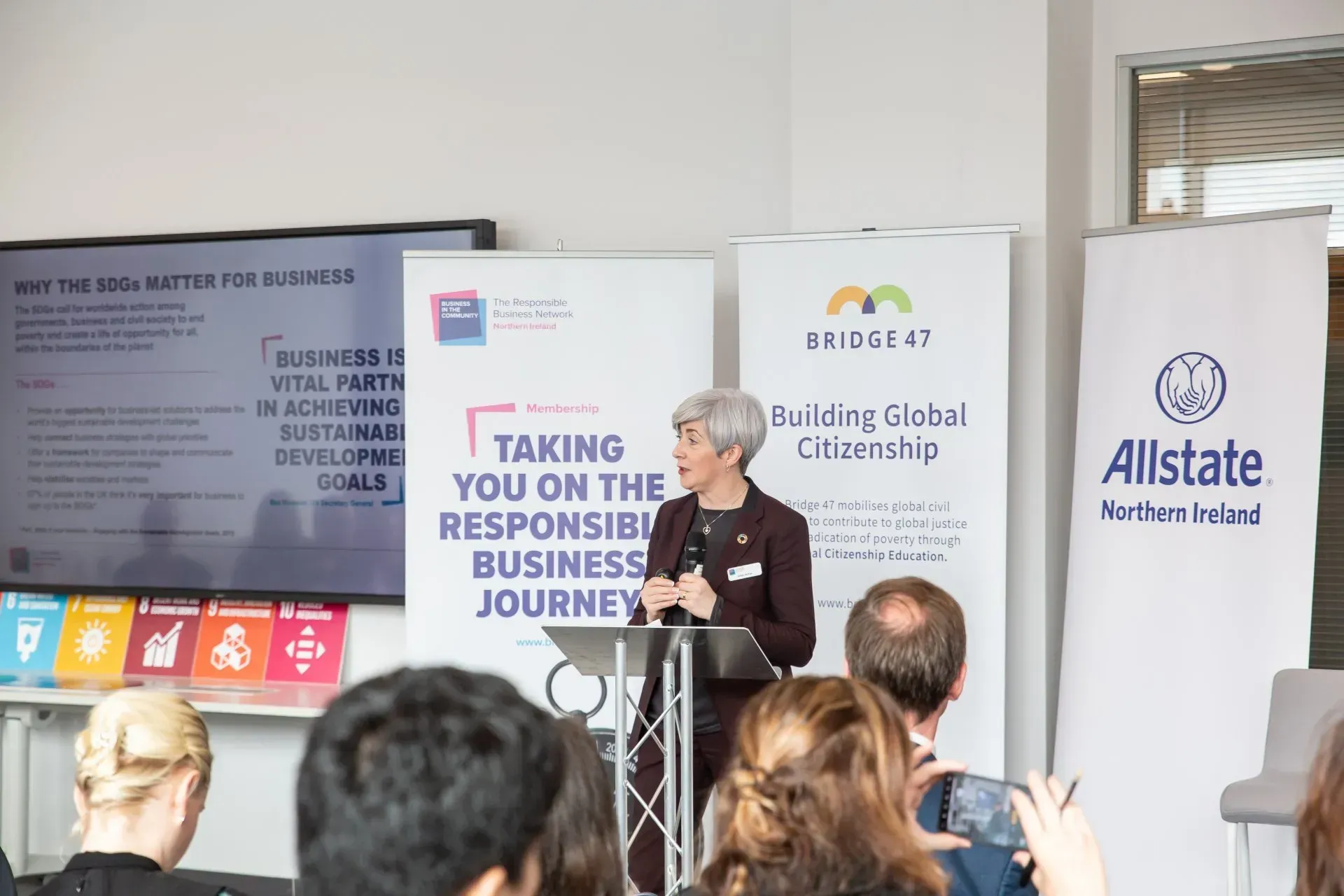 Speaker at podium in conference room with business event banners and audience listening