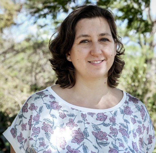 Smiling woman in a white floral top outdoors with trees in the background
