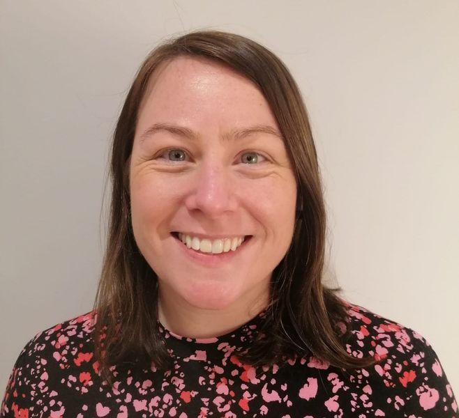Smiling woman with brown hair in a black floral top against a plain light wall