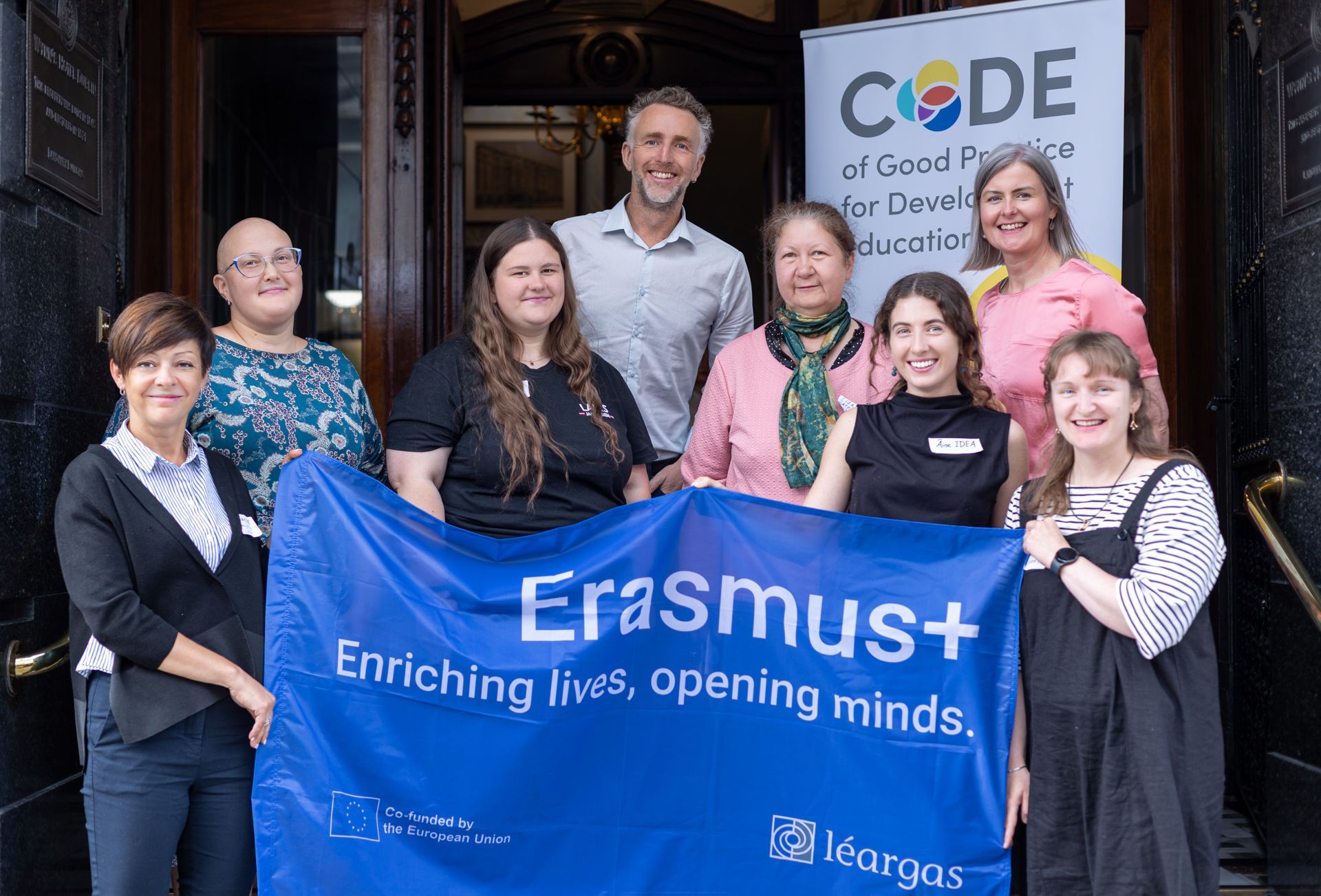 Group posing with an Erasmus+ banner in front of a CODE sign at an event