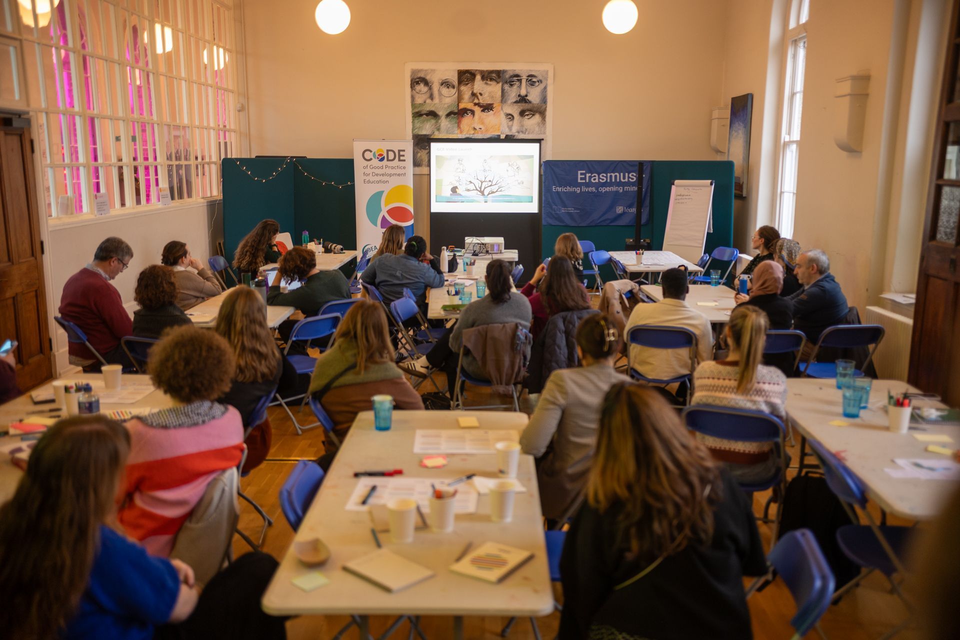 Conference audience seated in a hall, facing a presentation screen at the front.