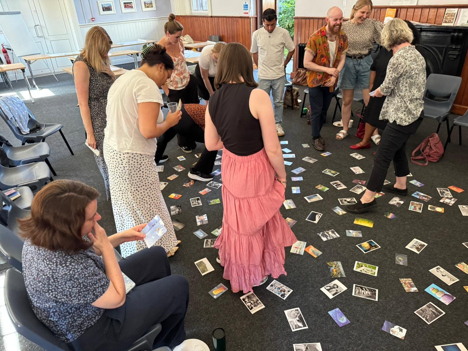 Group gathered around scattered cards on the floor in a bright room, discussing a floor activity.