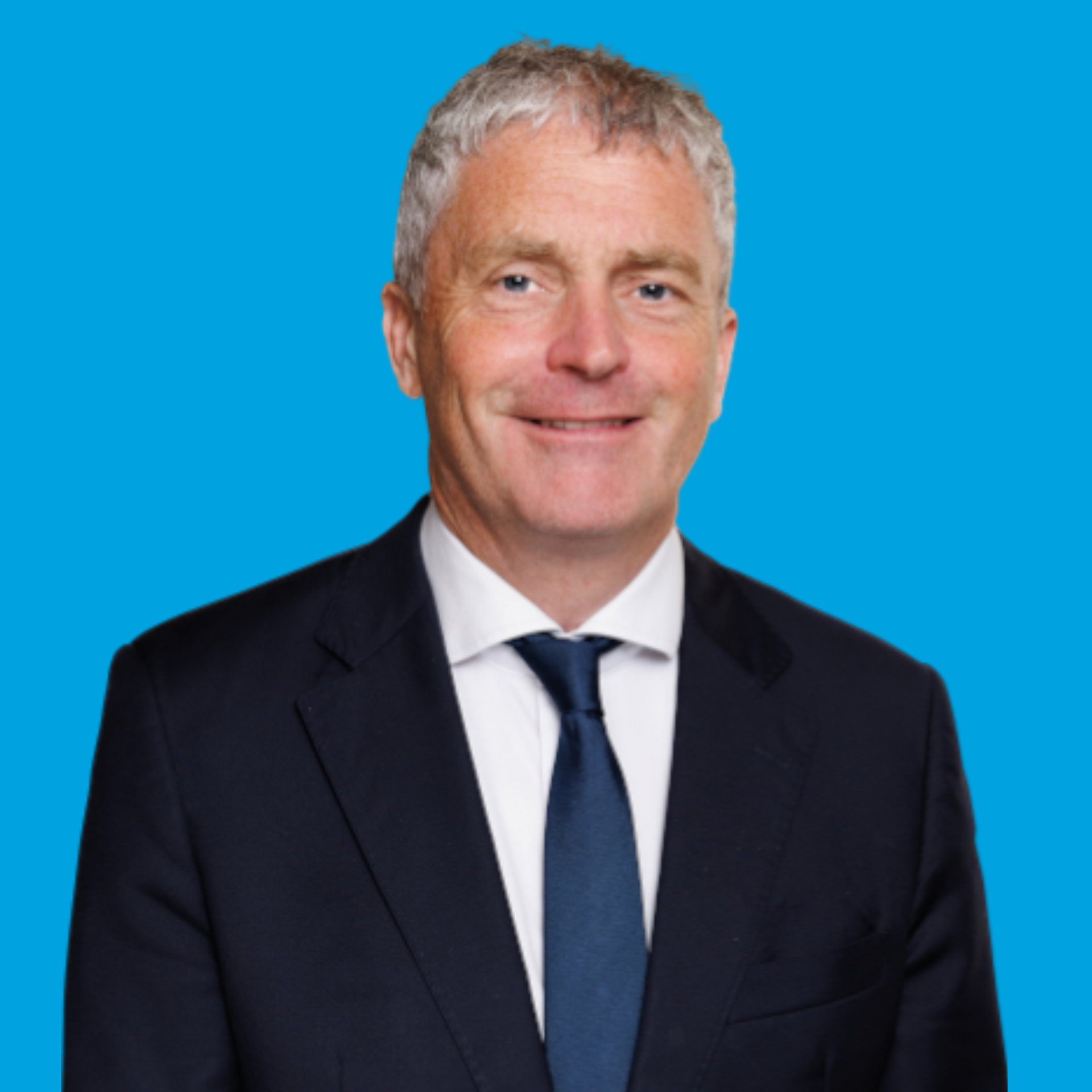 Portrait of a man in a dark suit and blue tie against a bright blue background