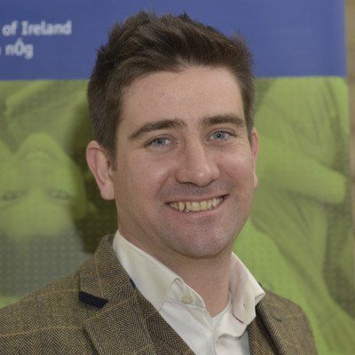 Smiling man in a tweed jacket before a blue and green backdrop