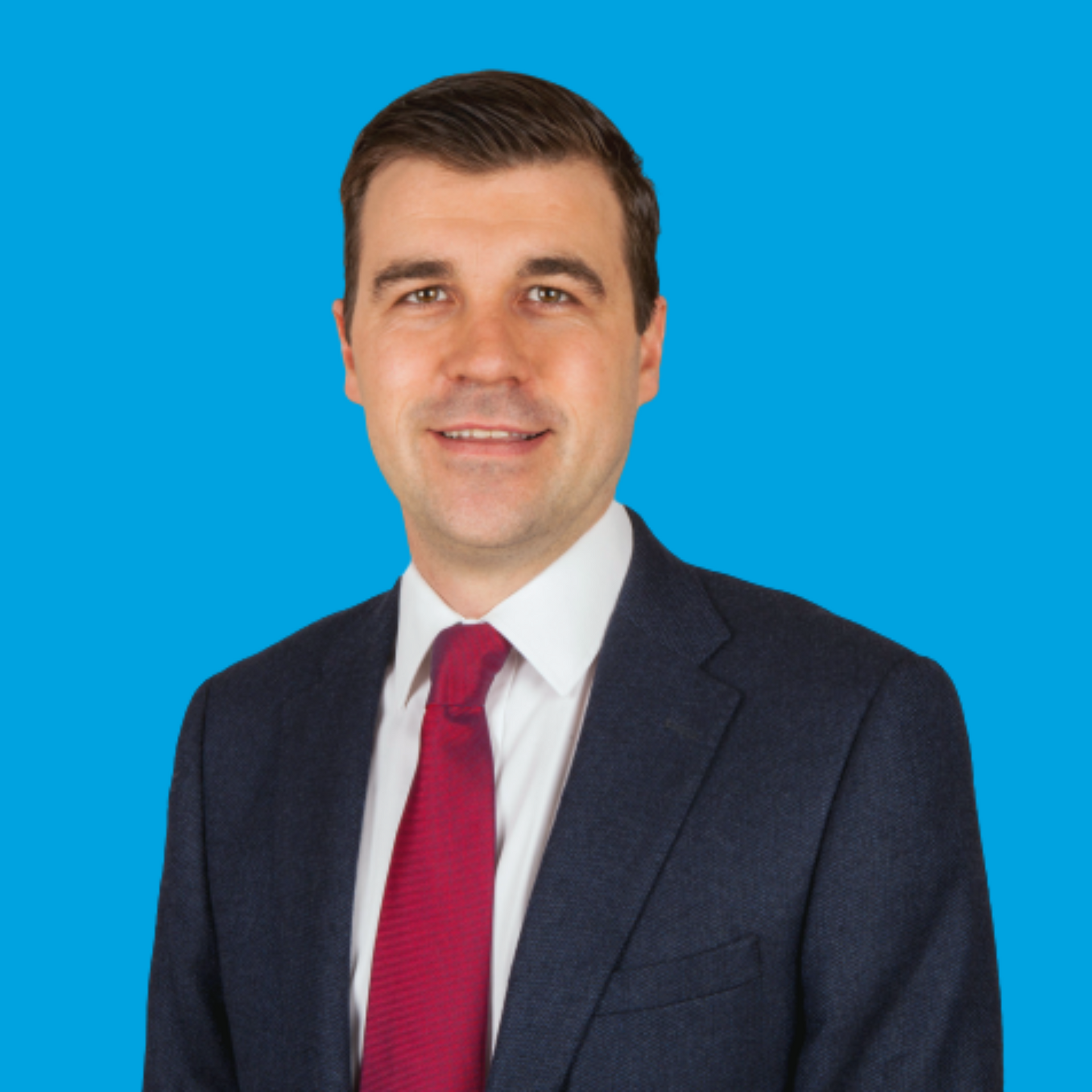 Man in a navy suit and red tie against a bright blue background