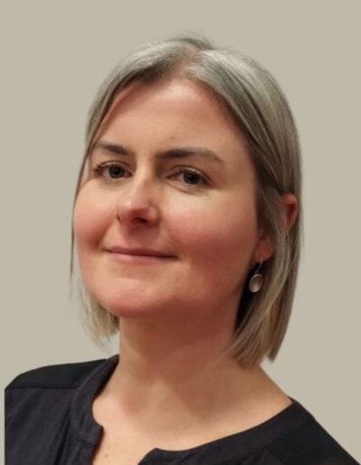 Portrait of a smiling person with short gray hair against a plain beige background