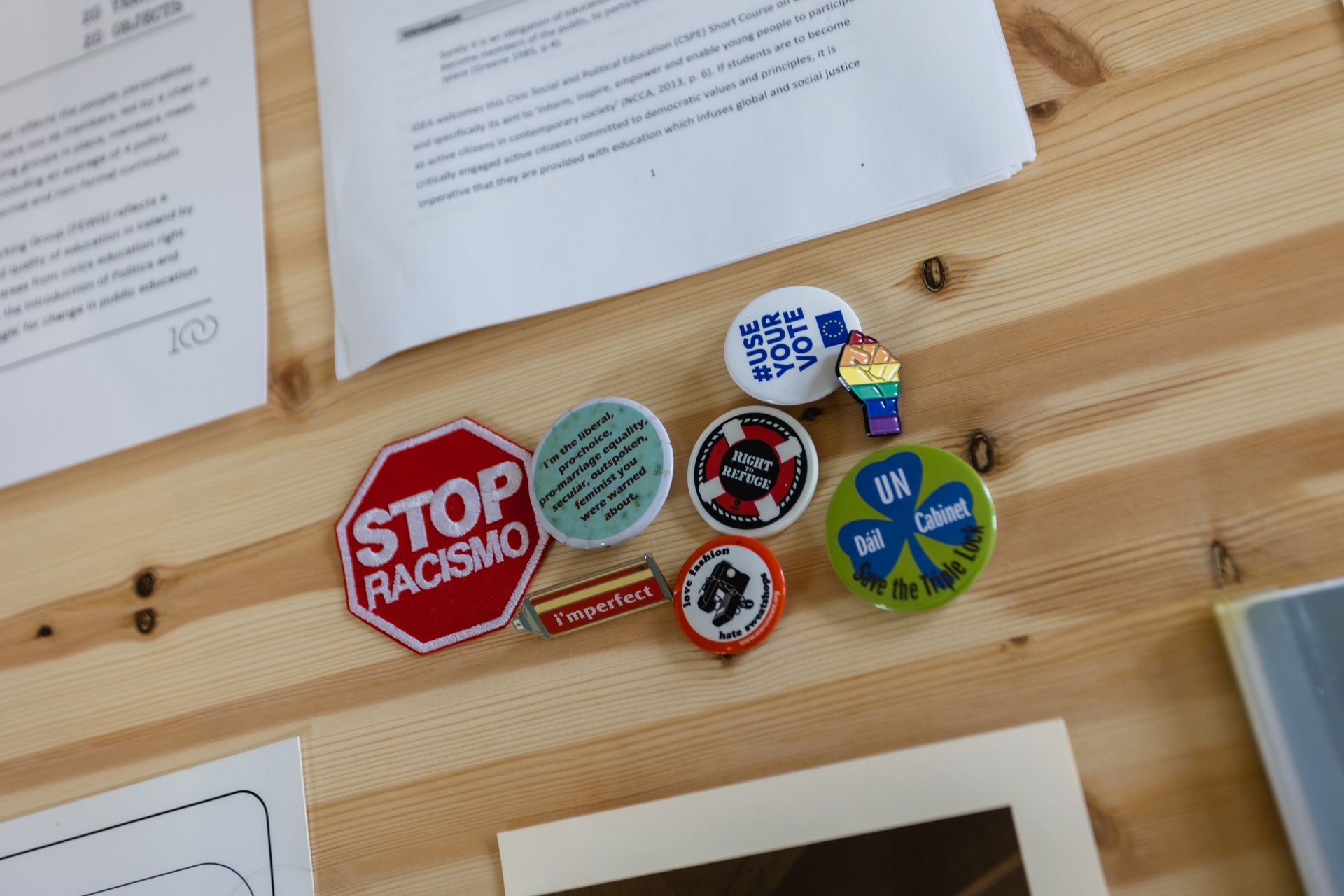 Assorted advocacy stickers on a wooden wall, including “STOP RACISM” and a green-blue peace symbol.