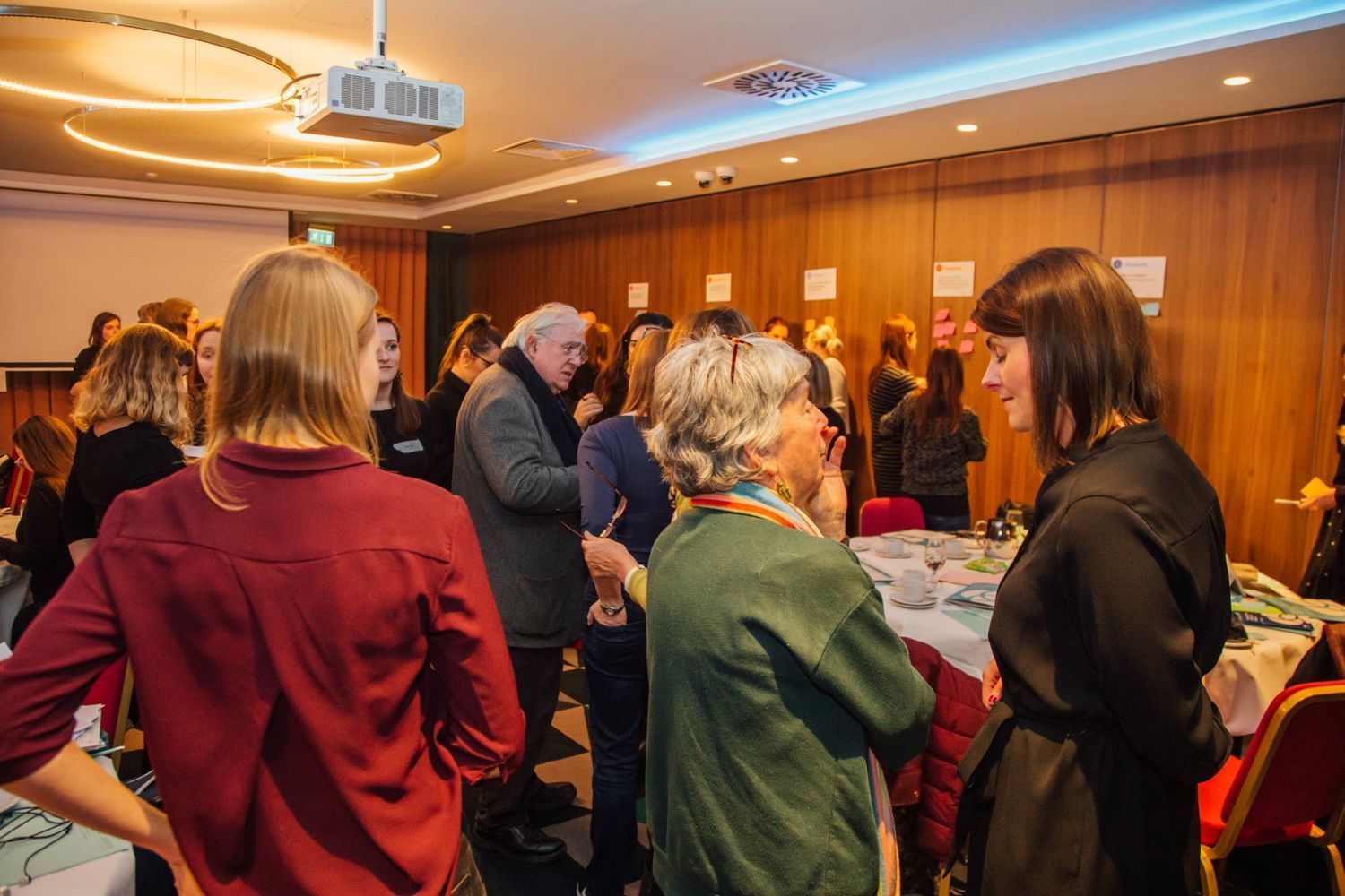 People mingling at a conference reception in a wood-paneled room with tables and warm lighting
