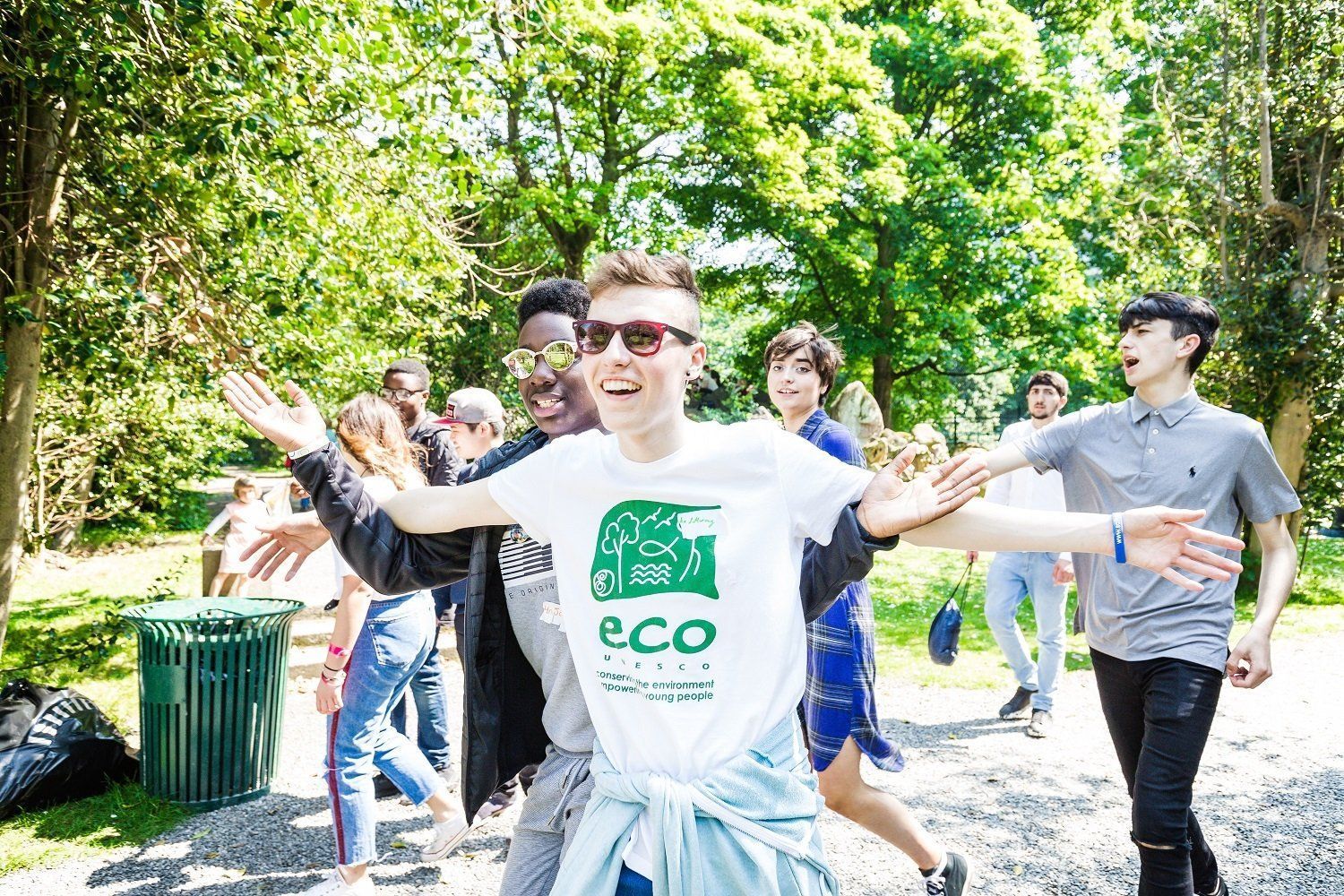 People dancing outdoors in a sunny park, with a smiling person in a white ECO shirt at center.