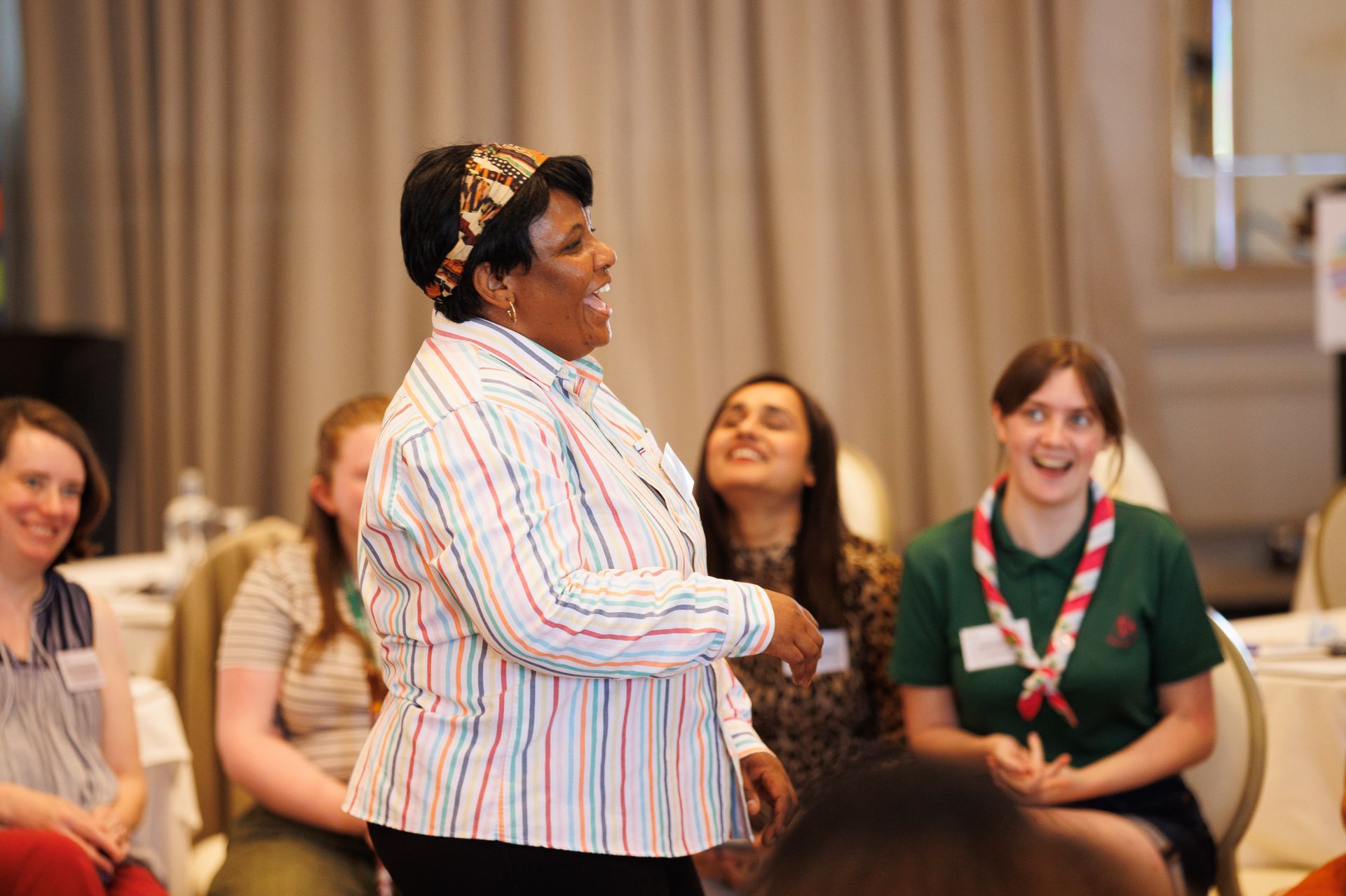 Speaker presenting to an audience in a conference room, with seated attendees smiling and listening