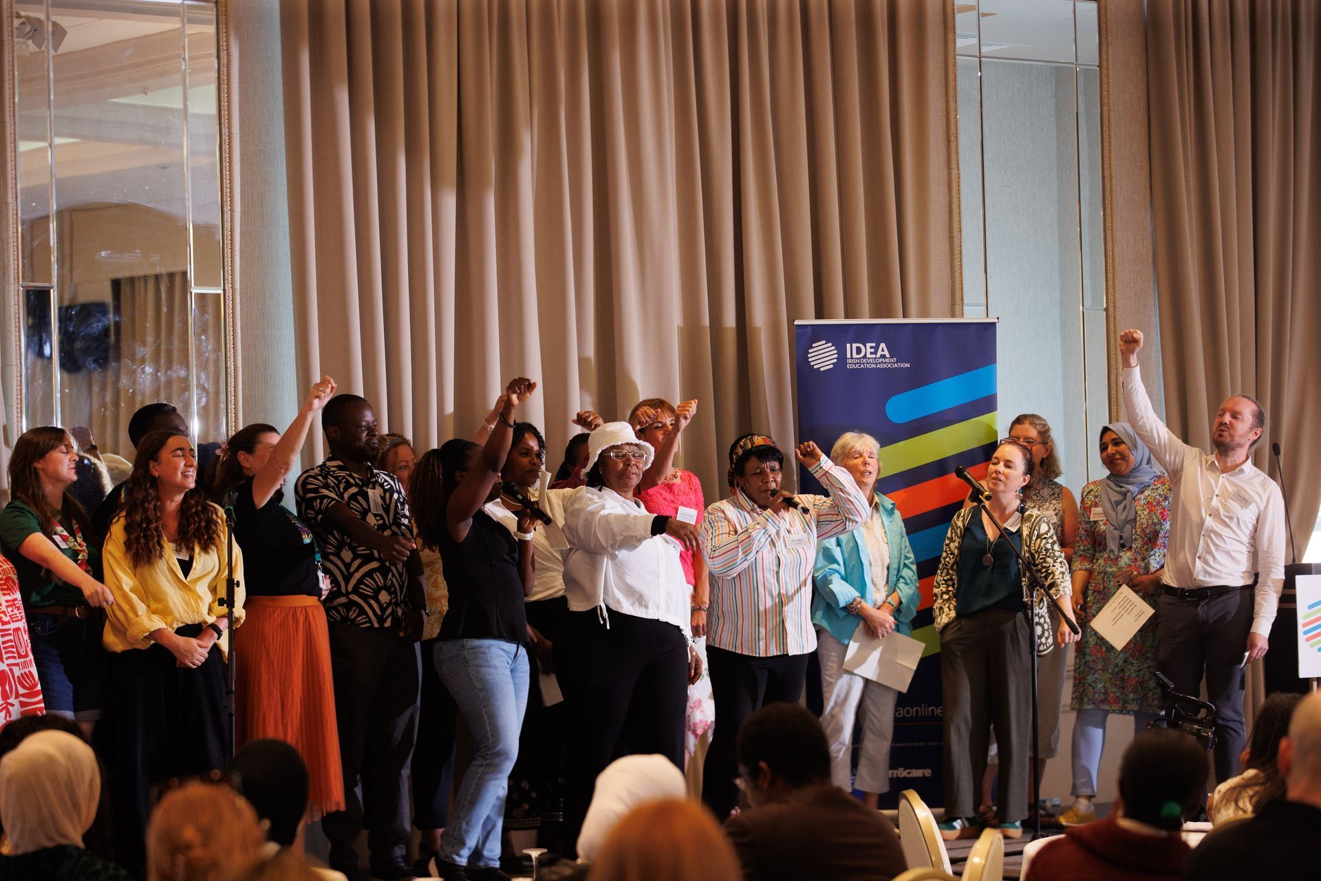 People on a stage raising their hands during a group performance or celebration in a curtained room