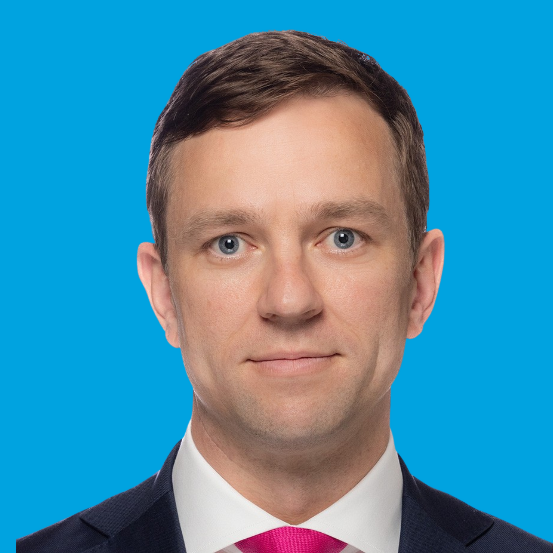 Studio headshot of a man in a dark suit and red tie on a bright blue background