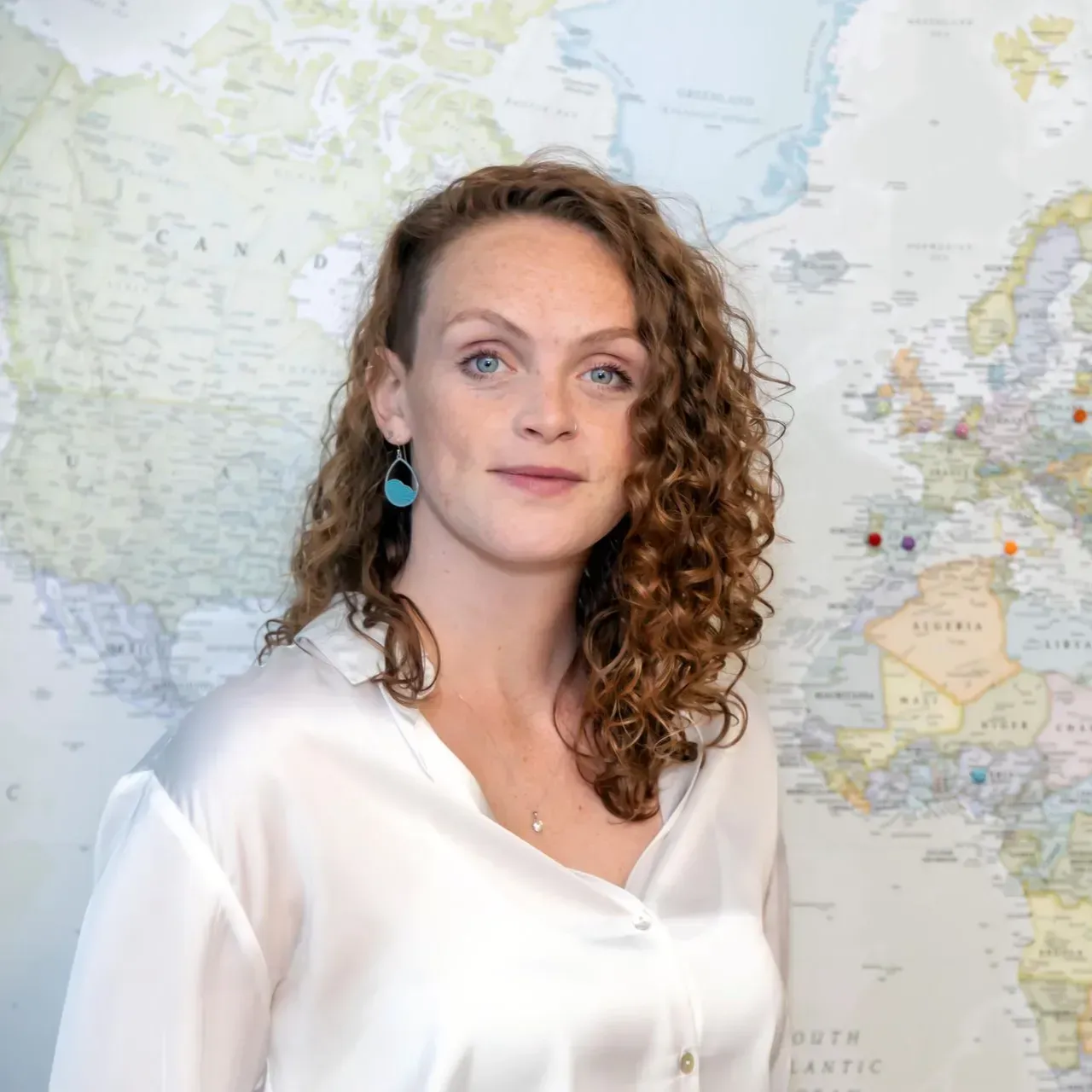 Woman in a white blouse standing before a world map backdrop, looking at the camera.