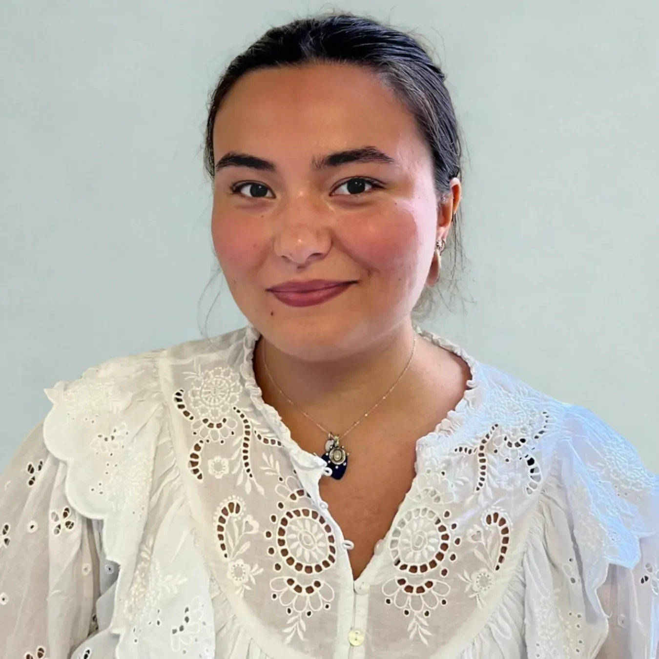 Smiling person in a white lace blouse against a plain light background