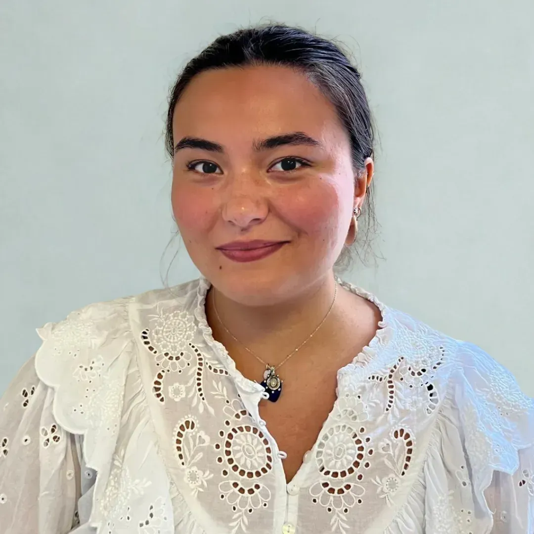Woman in a white lace blouse and necklace, smiling against a plain light background.
