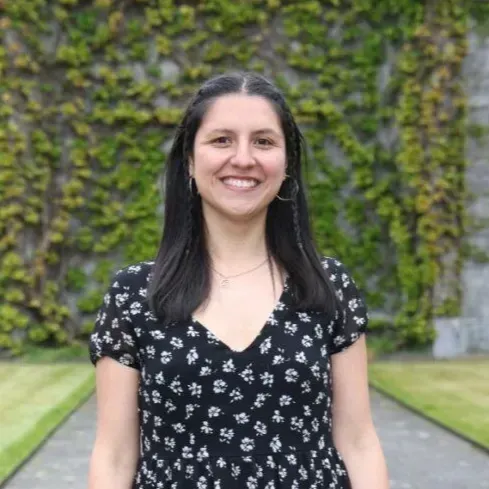 Smiling woman in a black floral dress standing outdoors on a tree-lined path