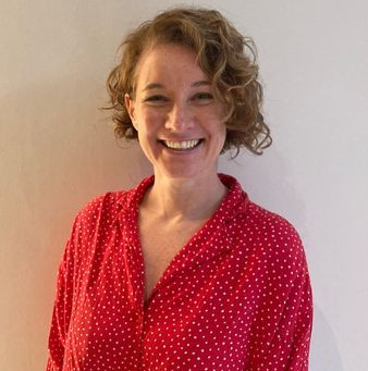 Smiling person in a red polka-dot blouse against a plain light background