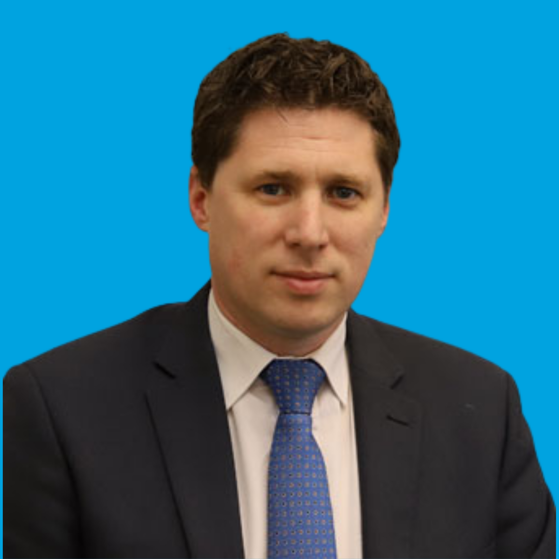 Man in a dark suit and blue tie against a solid blue background