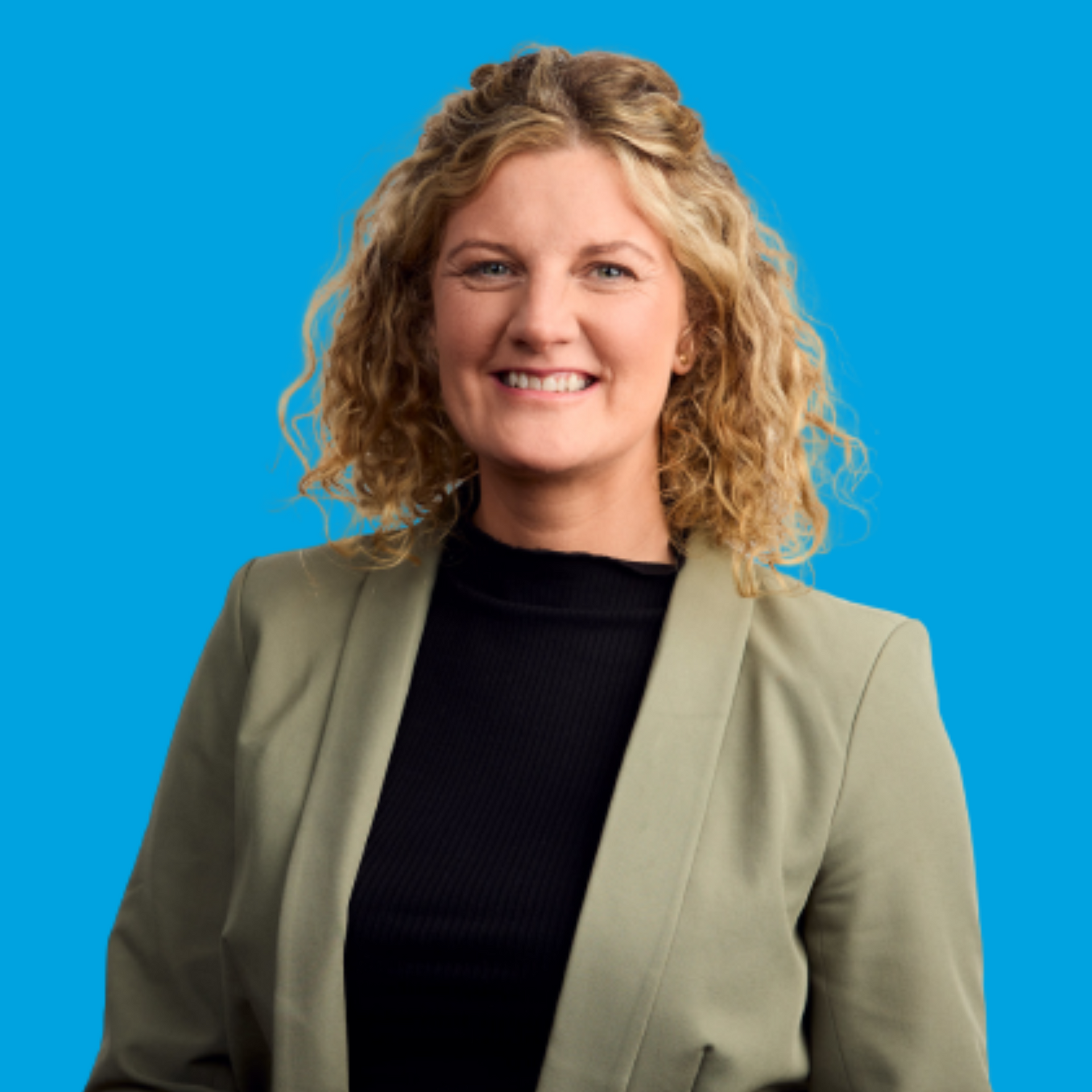 Smiling woman with curly blonde hair in a green blazer against a blue background