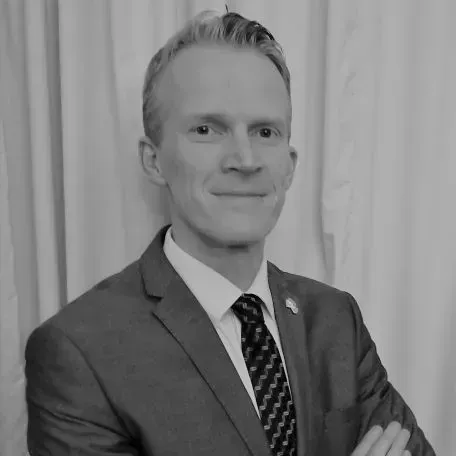 Portrait of a man in a suit and tie against a curtain backdrop, smiling slightly