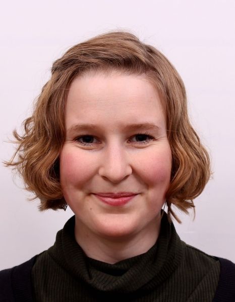 Portrait of a smiling person with short wavy hair against a light background