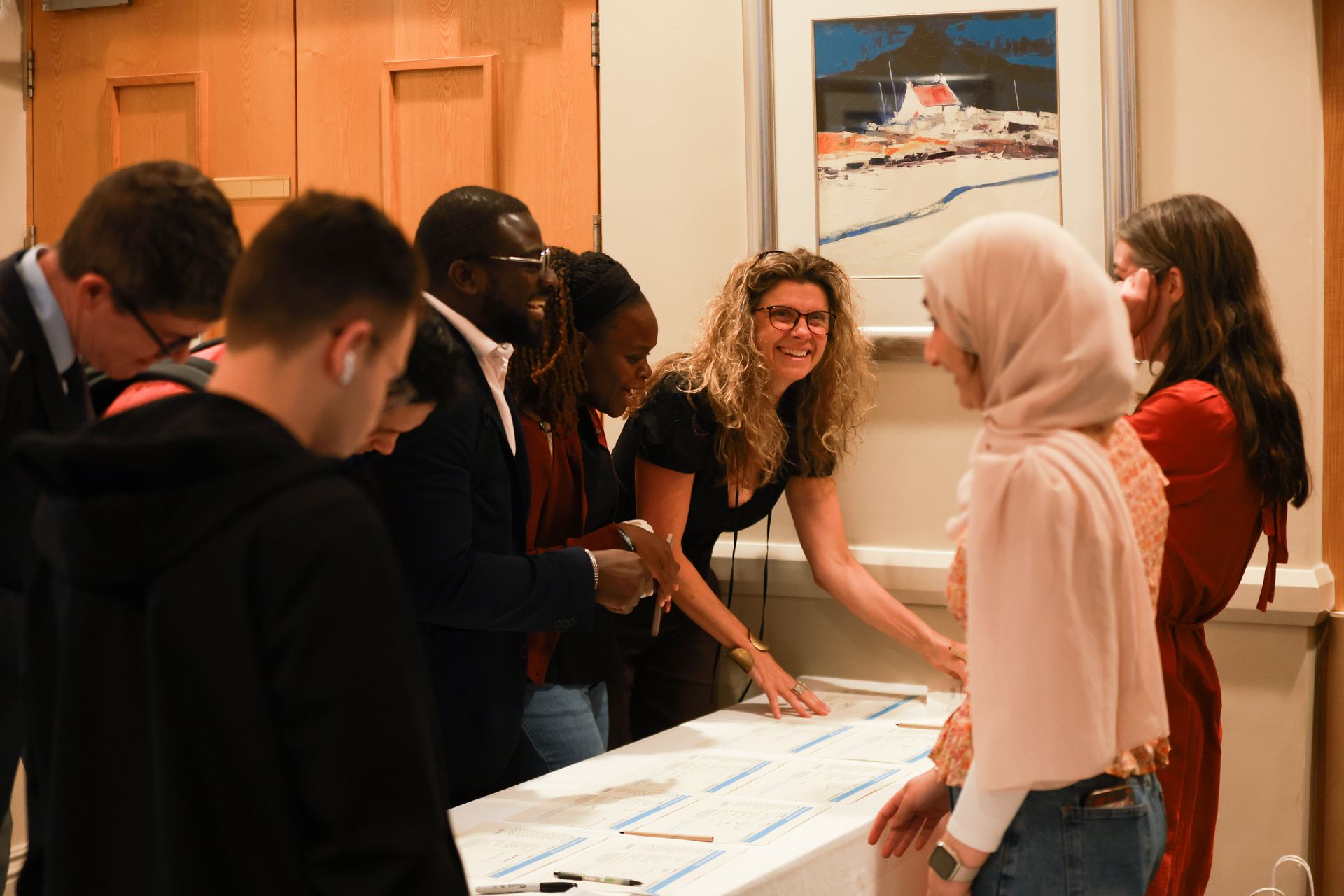 People gathered around a table examining large papers in a gallery-like room with framed artwork.
