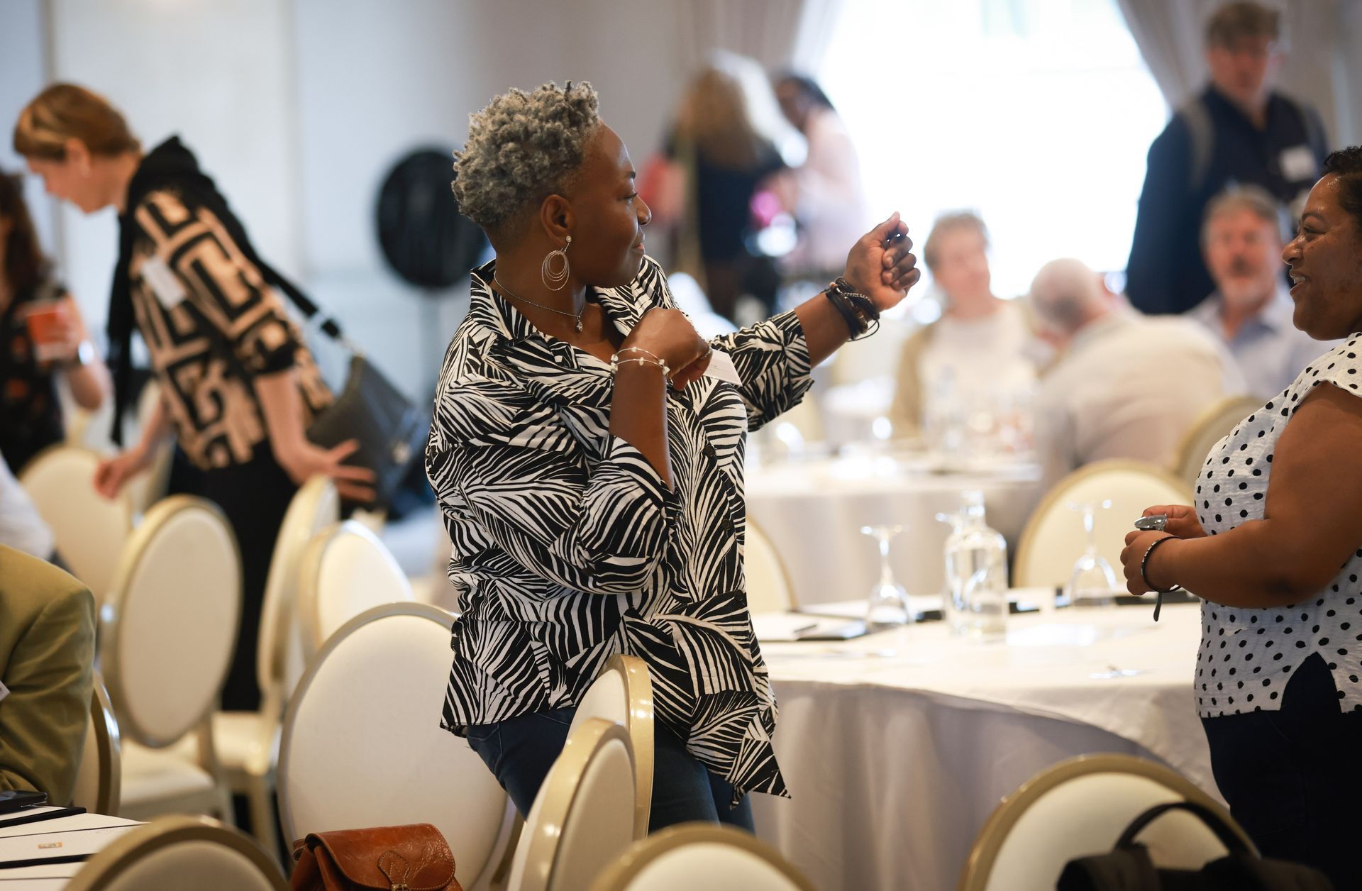 Woman speaking into a microphone at a banquet table in a bright dining hall