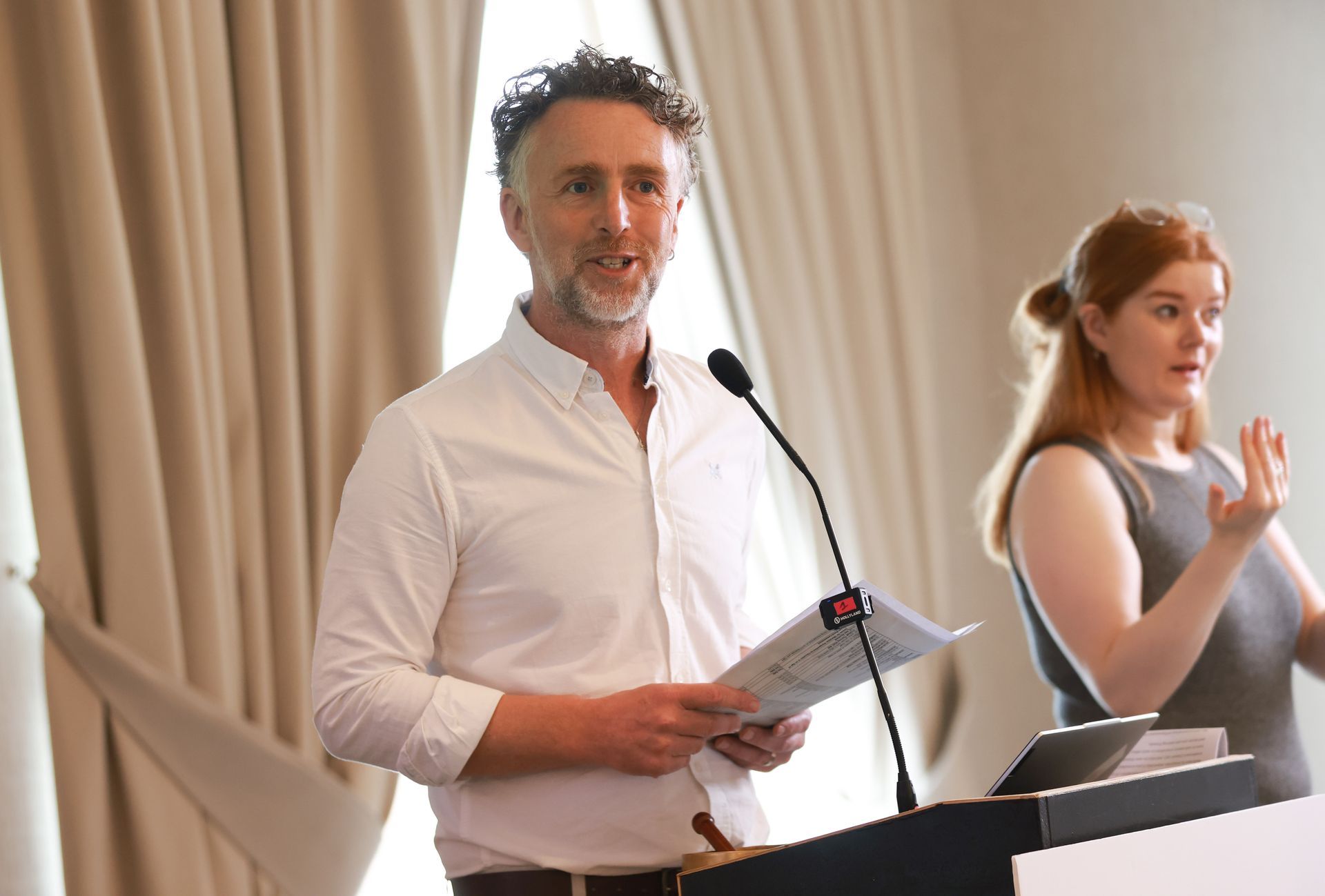 Man speaking at a podium with a microphone while a woman signs beside him on stage