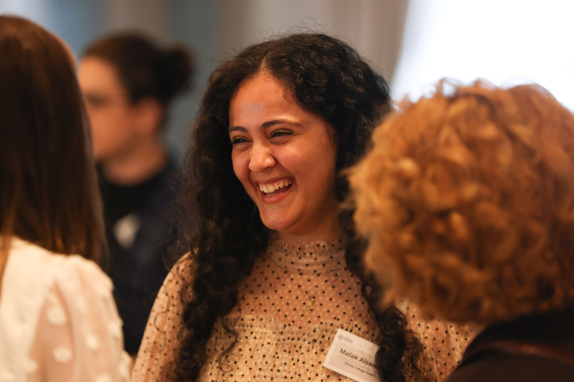 Three people chatting at an indoor event, with one woman smiling in the center.
