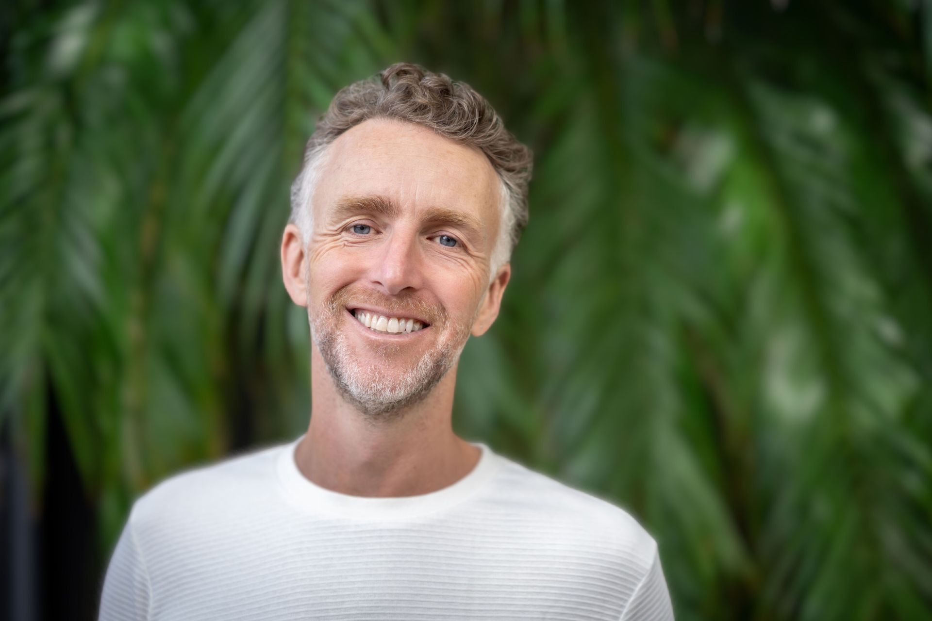 Smiling man in a white shirt standing before green foliage