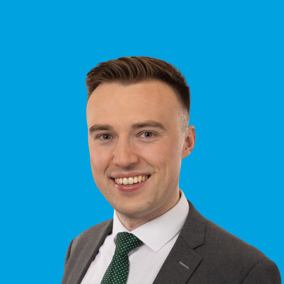 Smiling man in a suit and green tie against a bright blue background