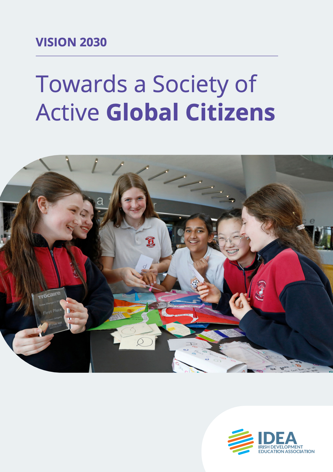 Students collaborating around colorful maps at a table with the title “Towards a Society of Active Global Citizens”