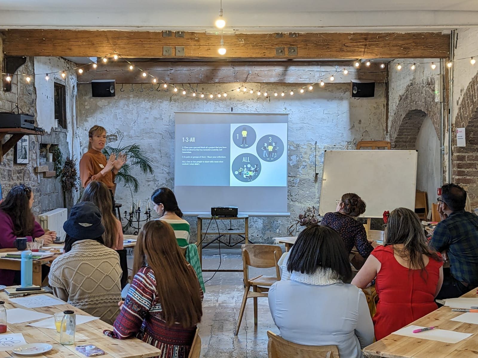 Workshop presentation in a rustic room, with a speaker and audience seated facing a projected slide.