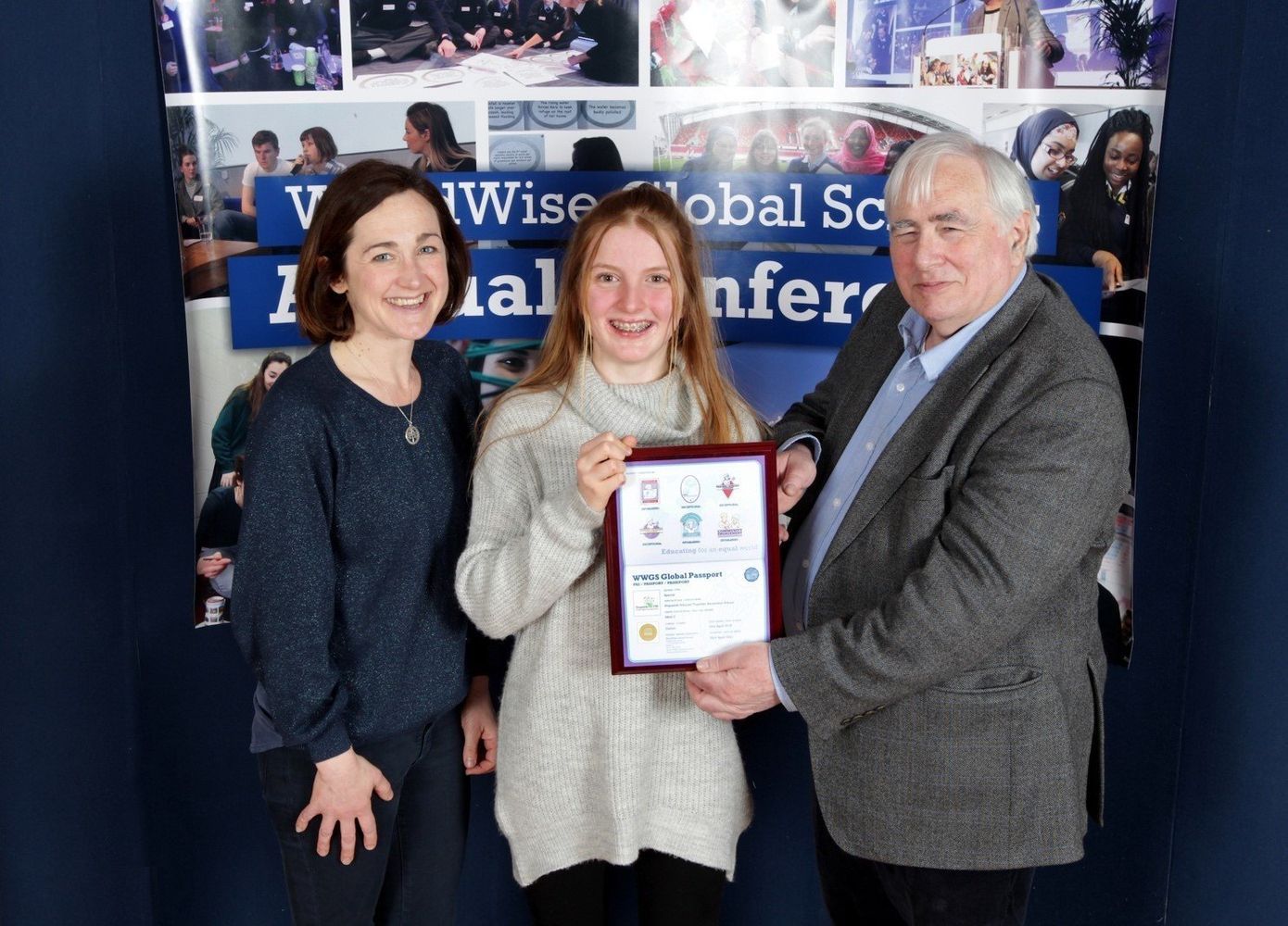 Three people posing at an awards event, holding a certificate in front of a conference banner.