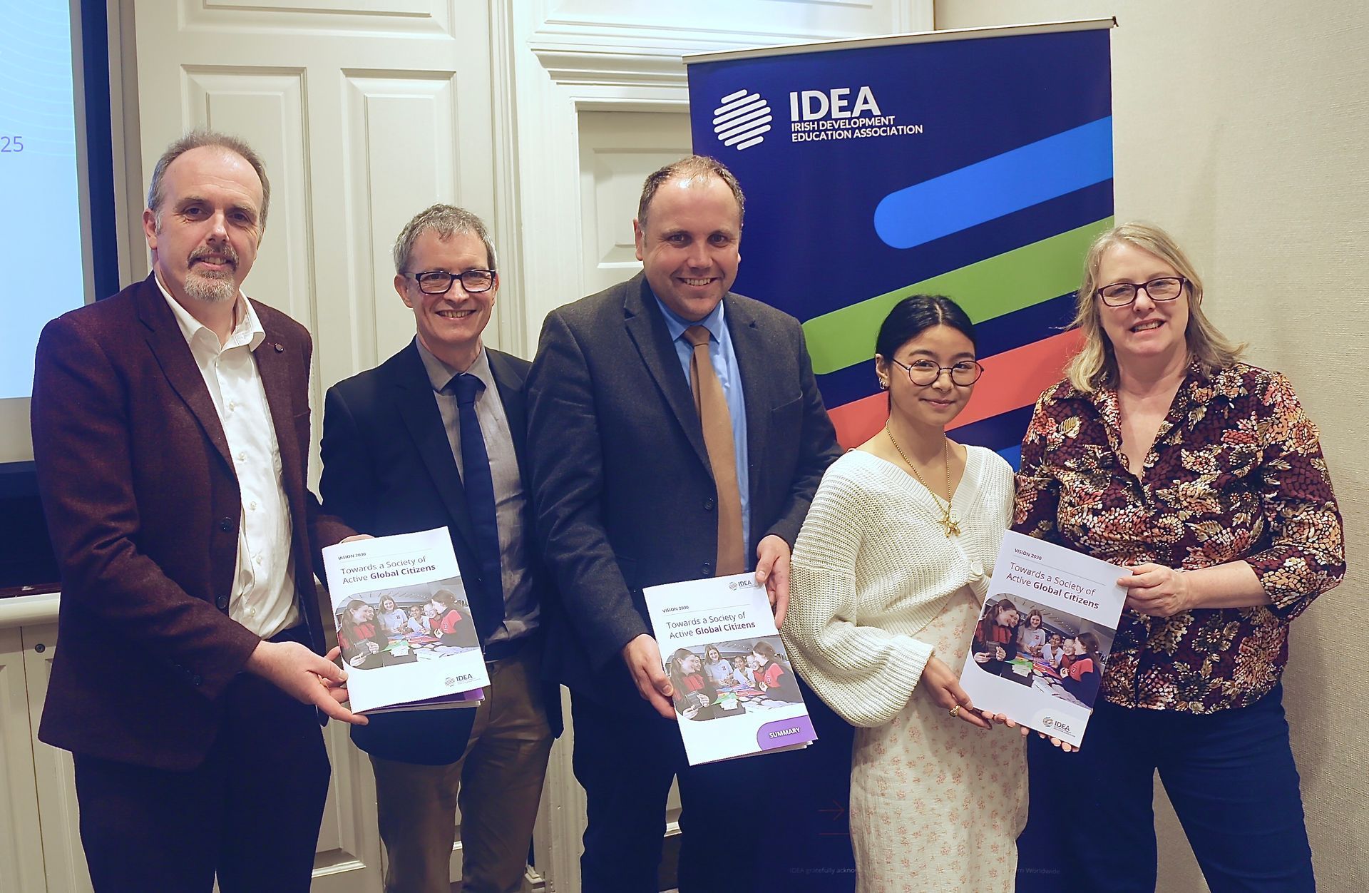Five people posing indoors holding reports beside an IDEA banner