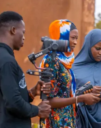 Three people outdoors, one holding a camera stabilizer and another checking a phone.