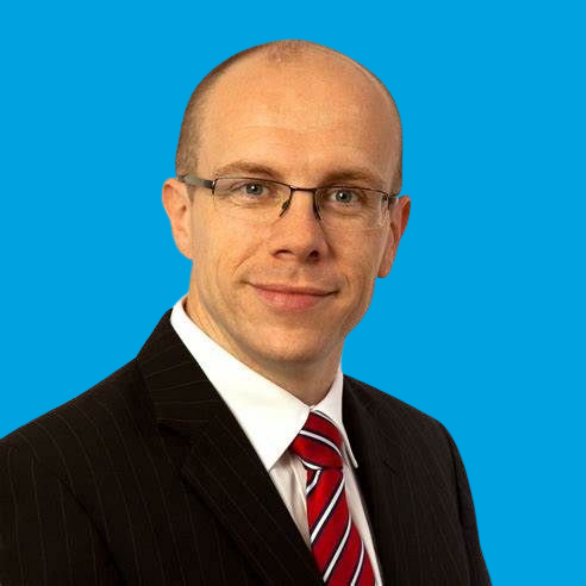 Portrait of a bald man in glasses wearing a dark suit and red striped tie against a blue background