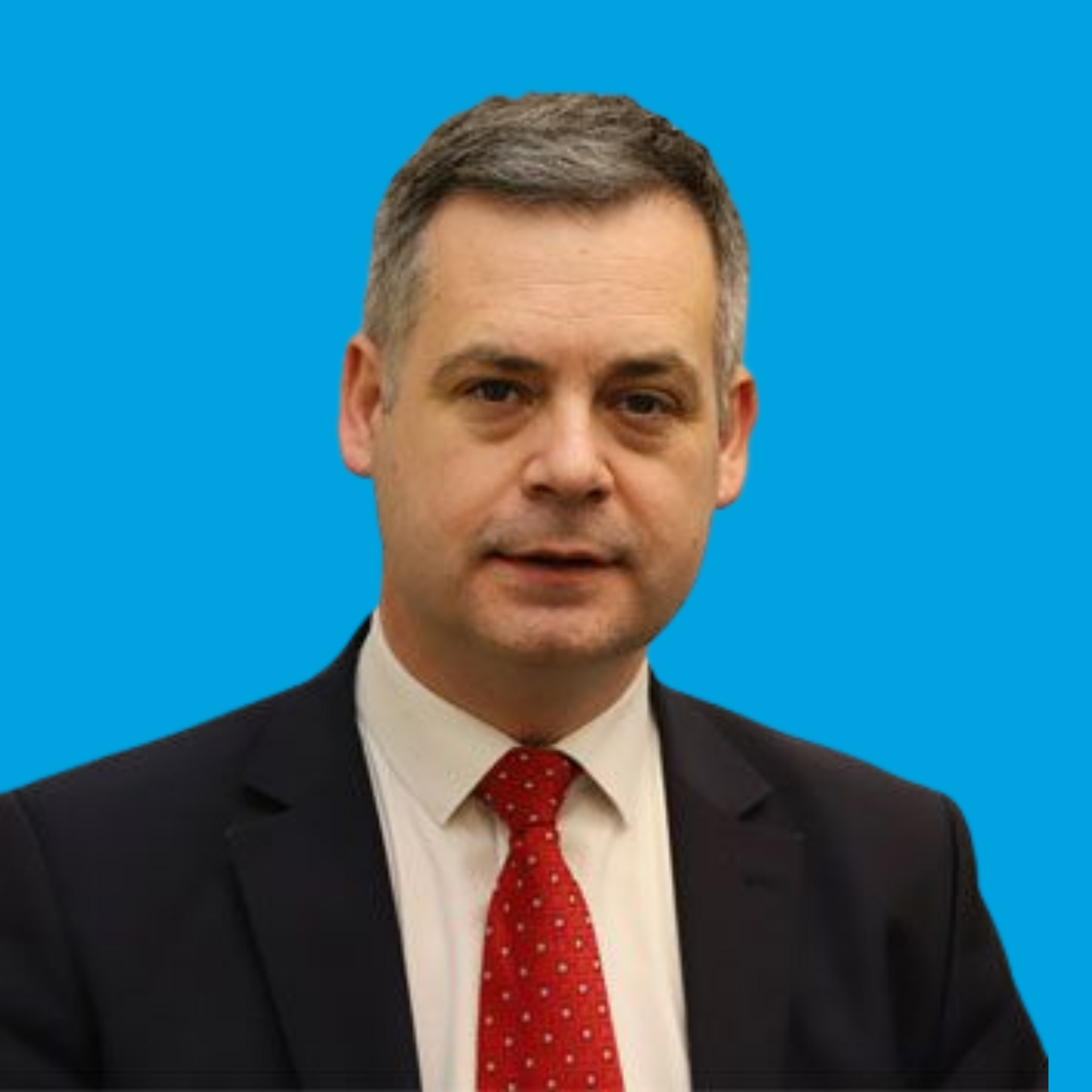 Man in a dark suit and red tie against a bright blue background