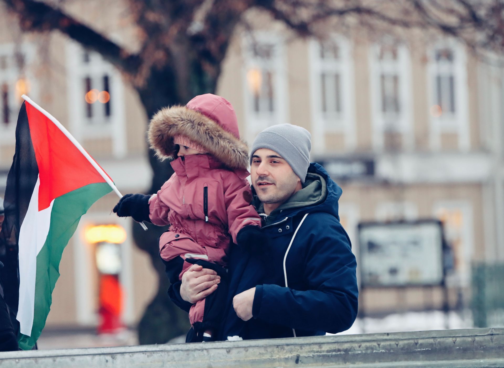 Man holding a child and a red, green, black, and white flag on a city street