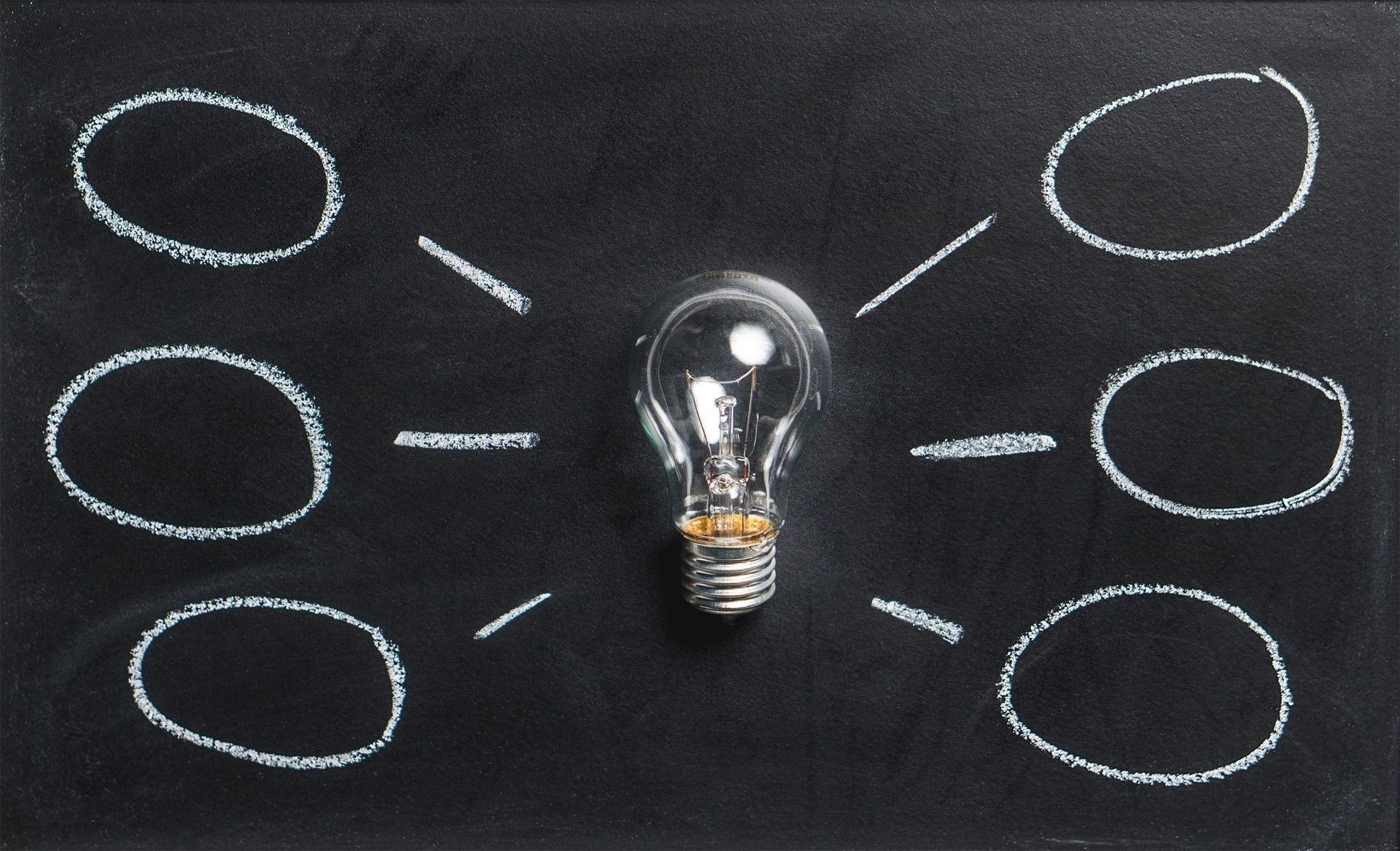 Light bulb centered on a chalkboard with six empty thought bubbles around it.