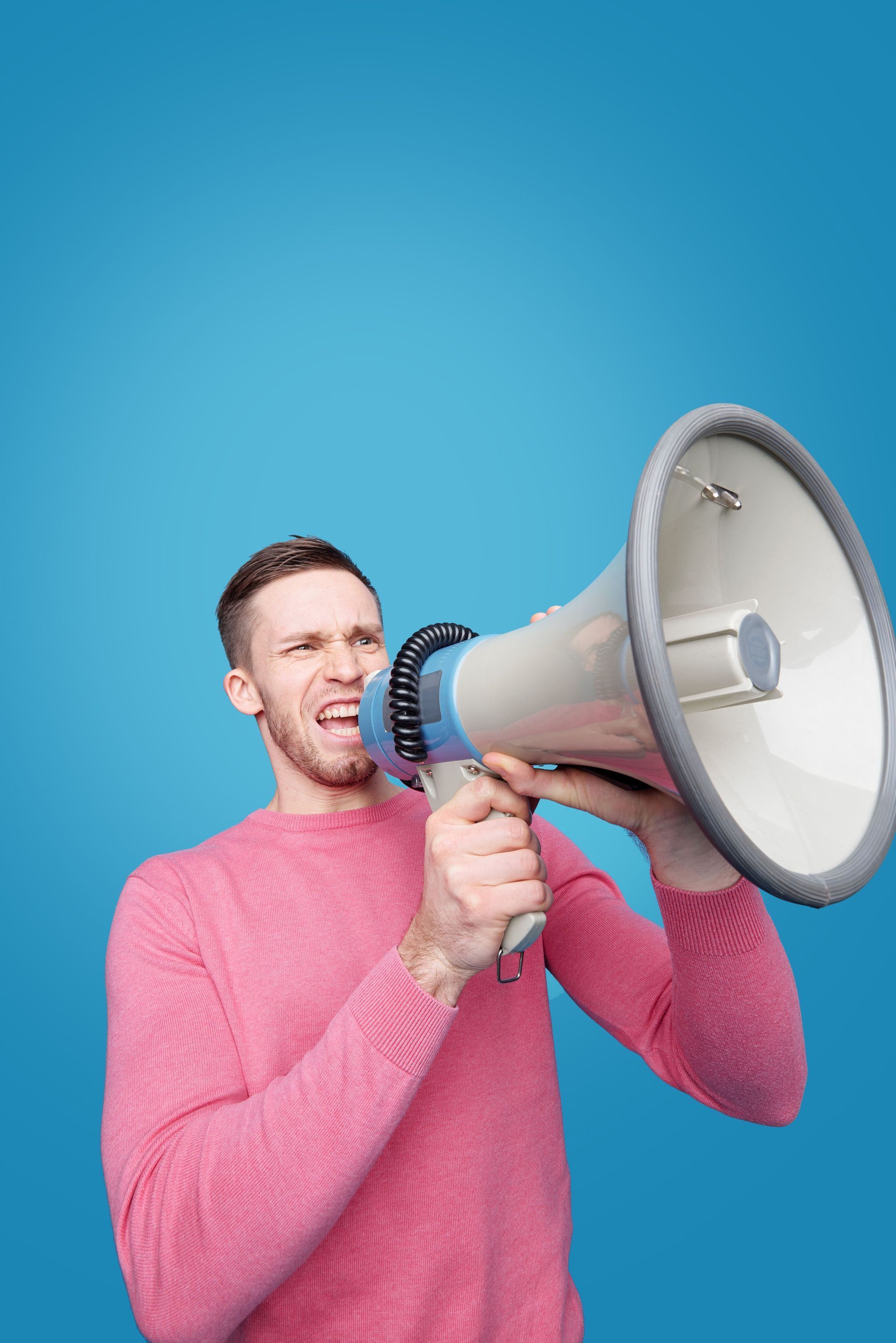 Man in a pink sweater speaking into a megaphone against a blue background