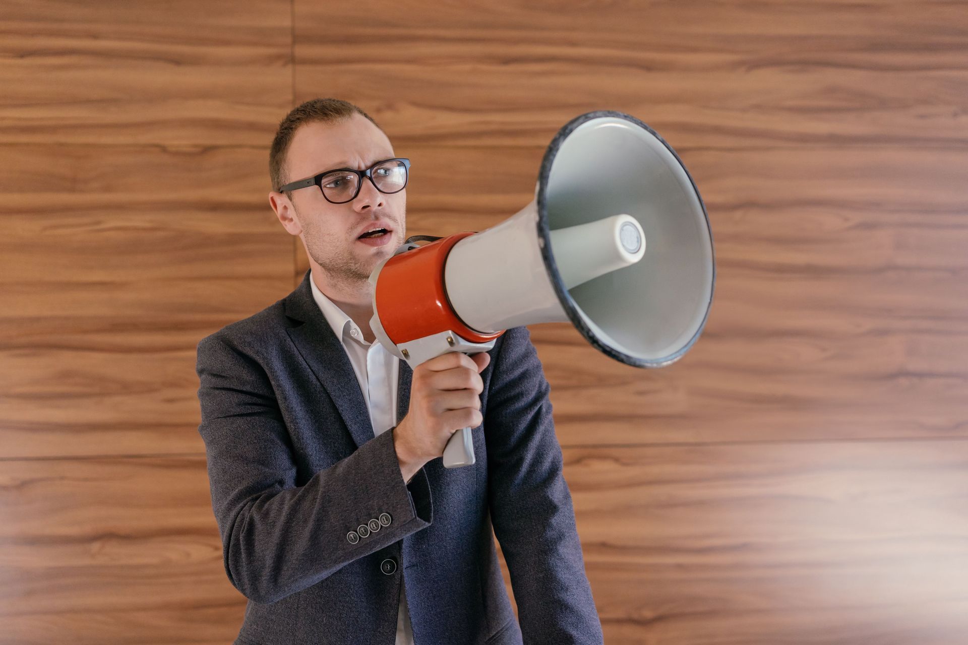 Man in a pink sweater speaking into a megaphone against a blue background