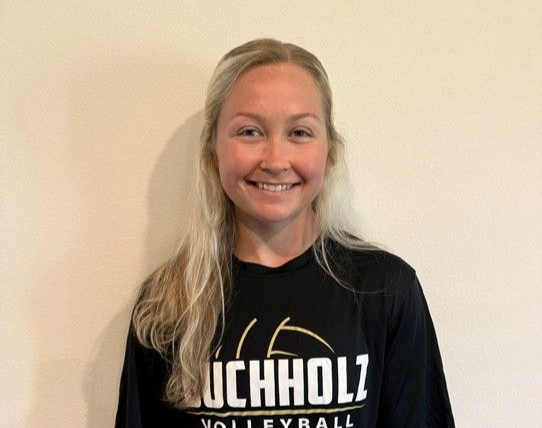 Smiling person in a black UCHHOLZ volleyball shirt against a plain beige wall