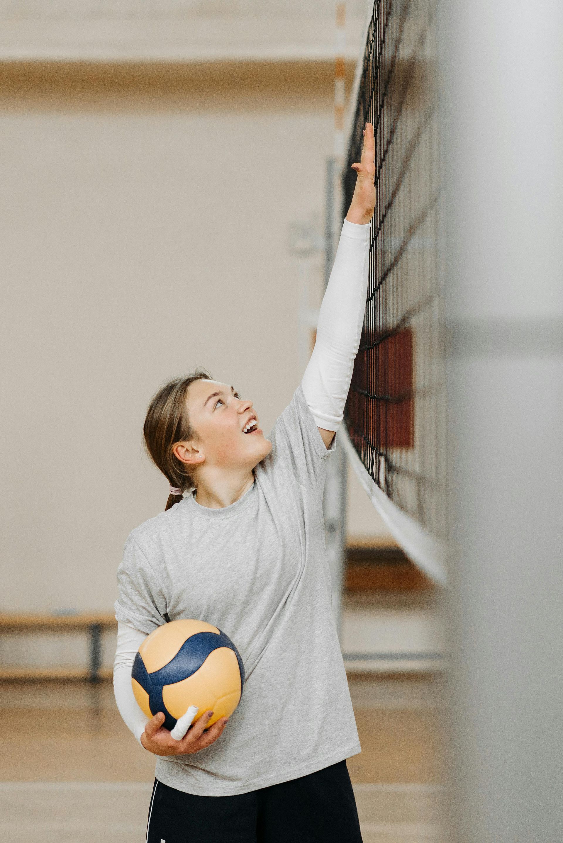 Volleyball player in gray shirt reaching up to block a ball at the net indoors