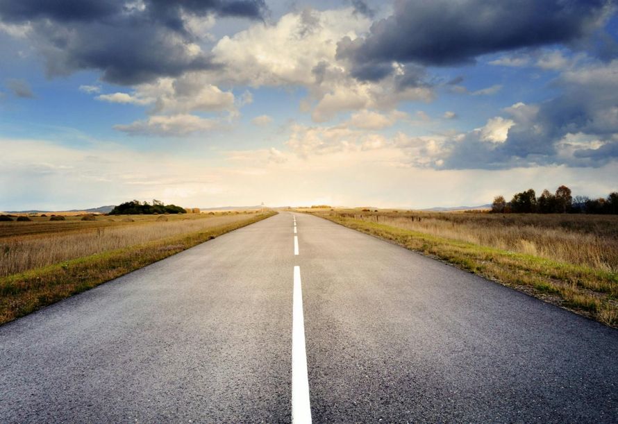 Empty rural road stretching toward the horizon under a cloudy sunset sky
